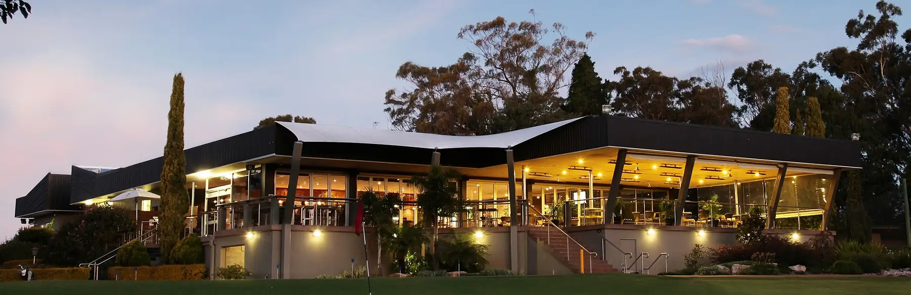 The clubhouse at twilight, its long veranda lit and the last golfers coming in