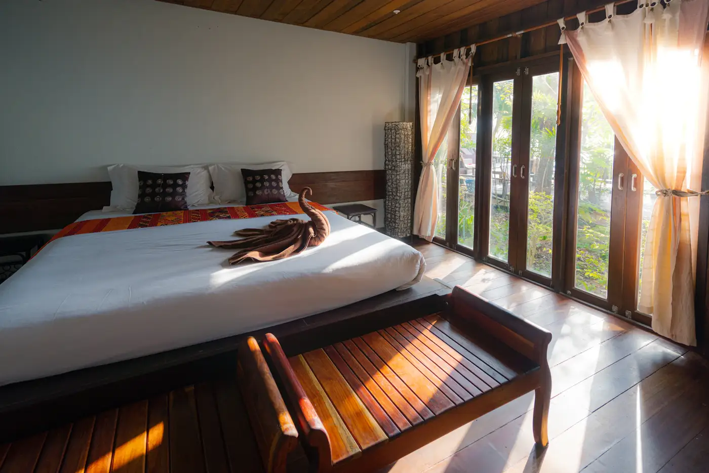 A guest cottage bedroom in warm wood and ivory linen, evening light through the drapes