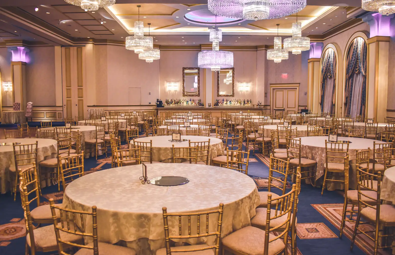 The Ballroom set for a wedding: round tables in ivory linen, garden flowers, tall windows open to the lawn