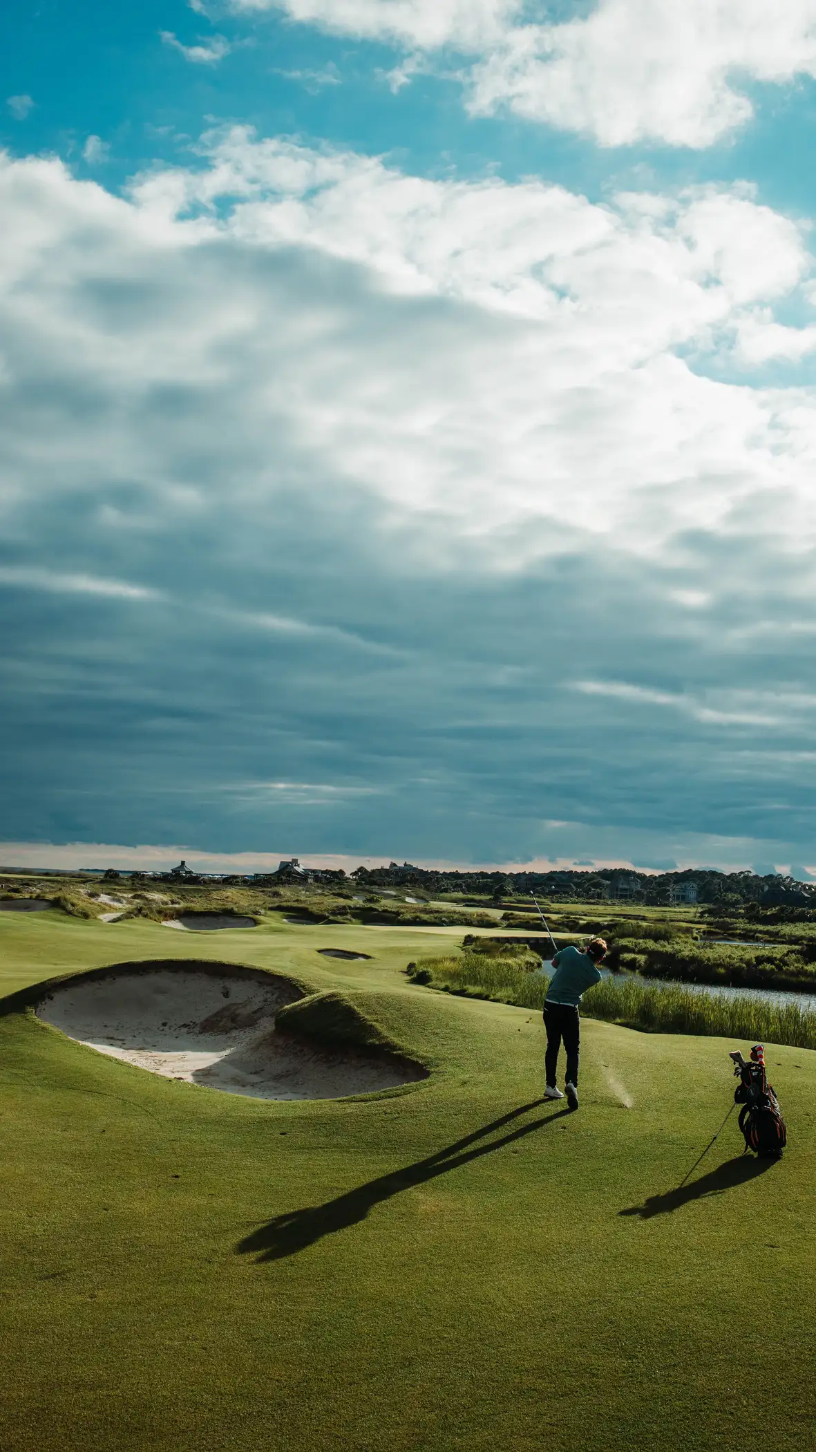 The eighteenth fairway at dusk, two members walking home past the great cross bunker