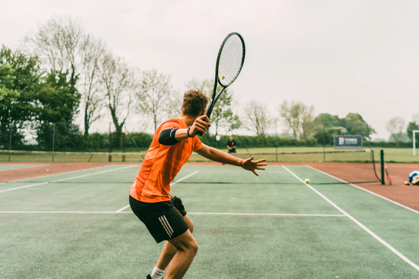 A Har-Tru clay tennis court brushed to a clean line, net taut, oaks beyond the fence